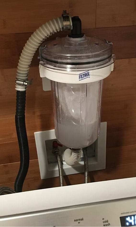 A laundry filter mounted above a laundry wall box, the bag inside visibly loaded with captured lint