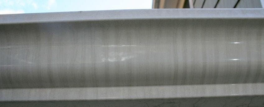 A long run of white aluminum gutter face marked with the evenly spaced vertical gray bands of tiger striping