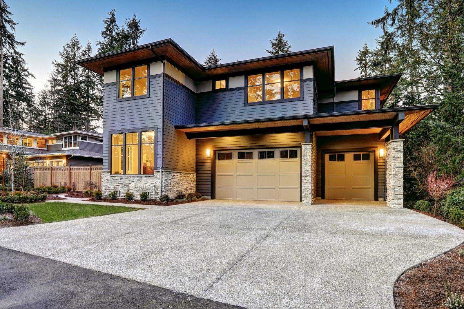 A modern Pacific Northwest home at twilight with warm interior lights on and a clean driveway, photographed listing-ready