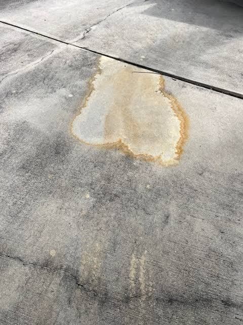 A battery acid stain on concrete: a pale etched footprint ringed by orange iron staining