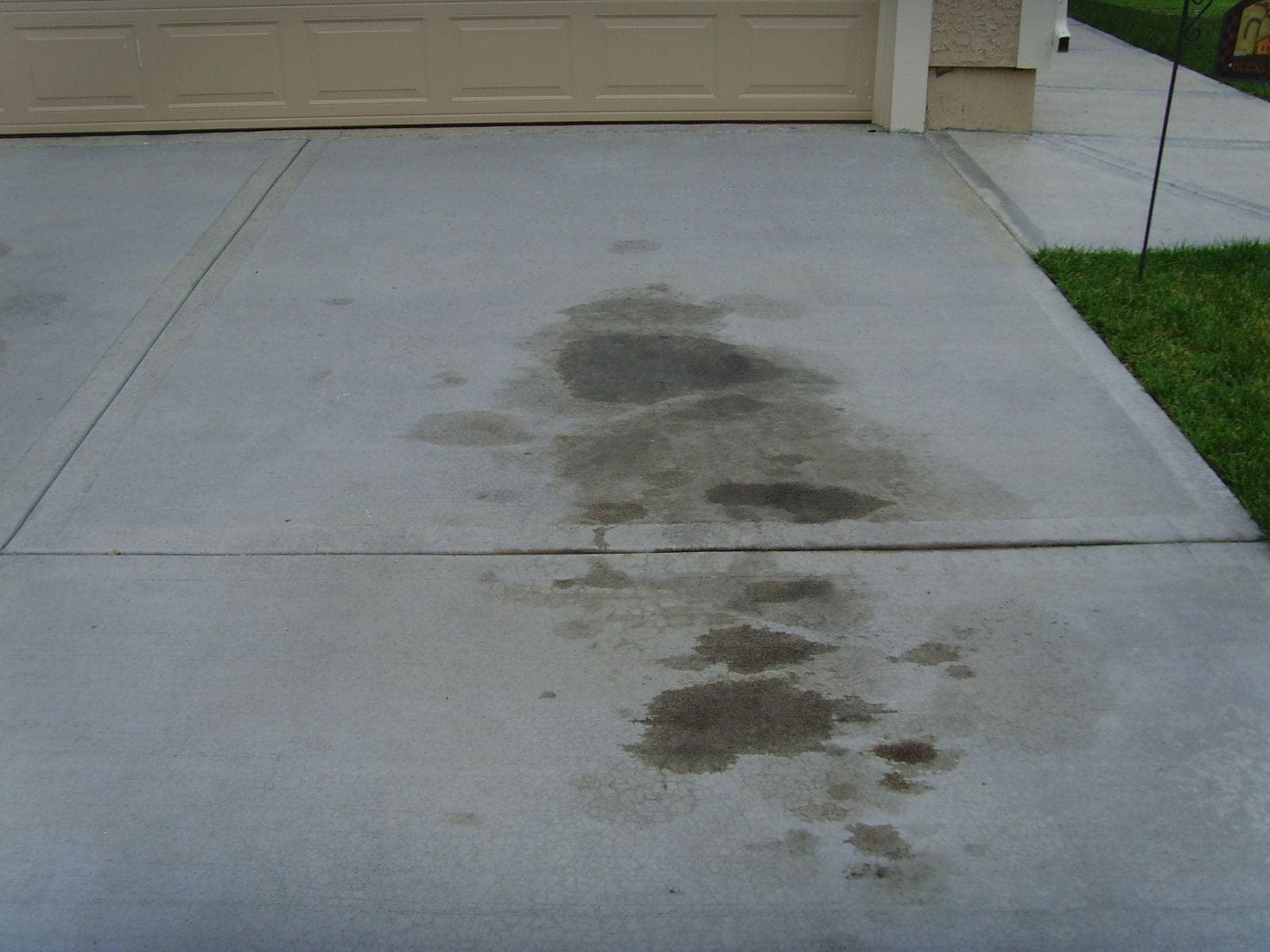 Dark oil drip stains soaked into the concrete of a driveway in front of a garage