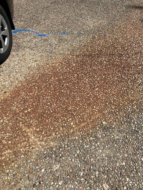 Rust bleeding in a broad orange stain across an exposed aggregate driveway