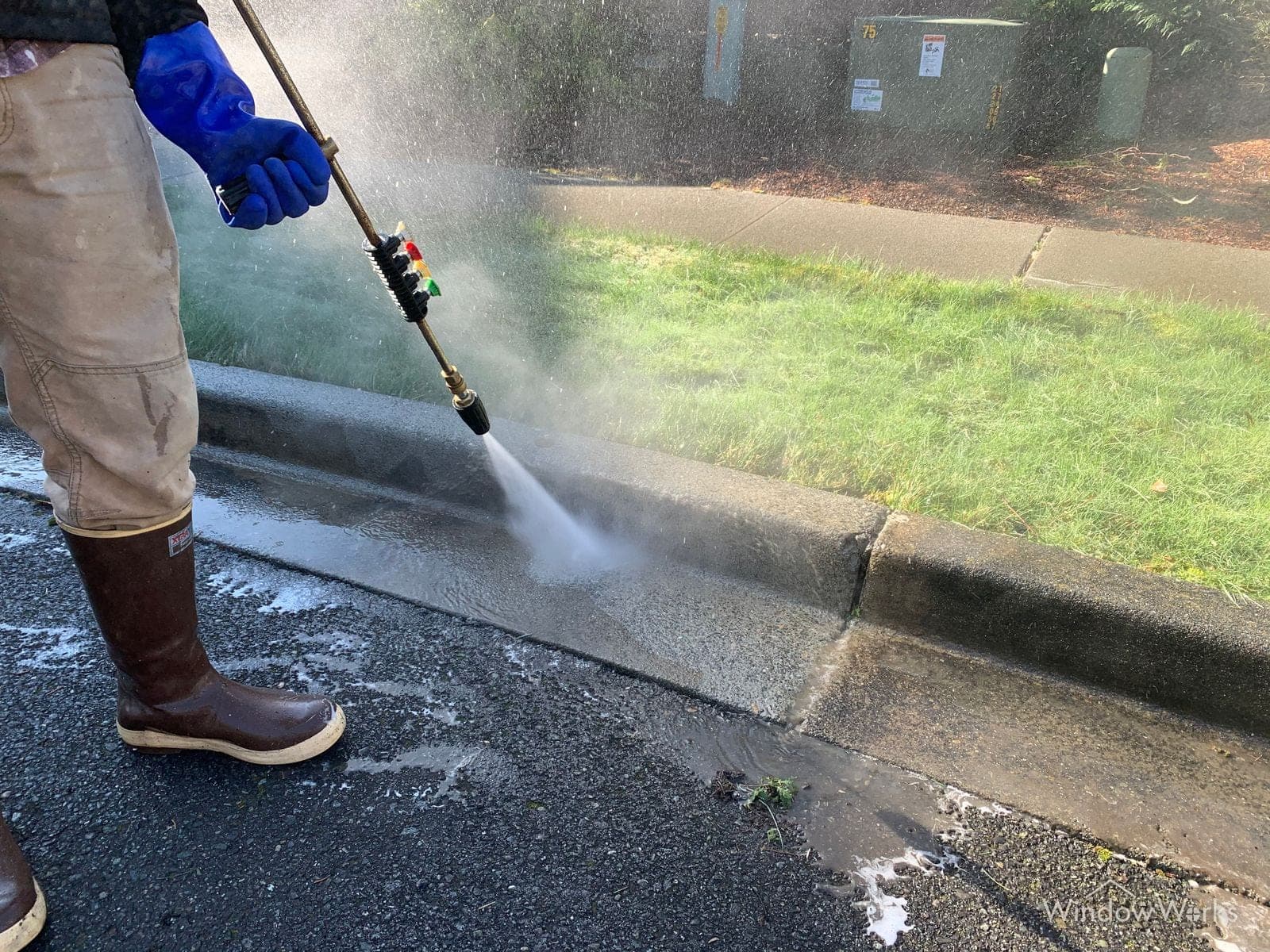 A WindowWorks technician treating a concrete curb line at low pressure, suds sheeting across the surface