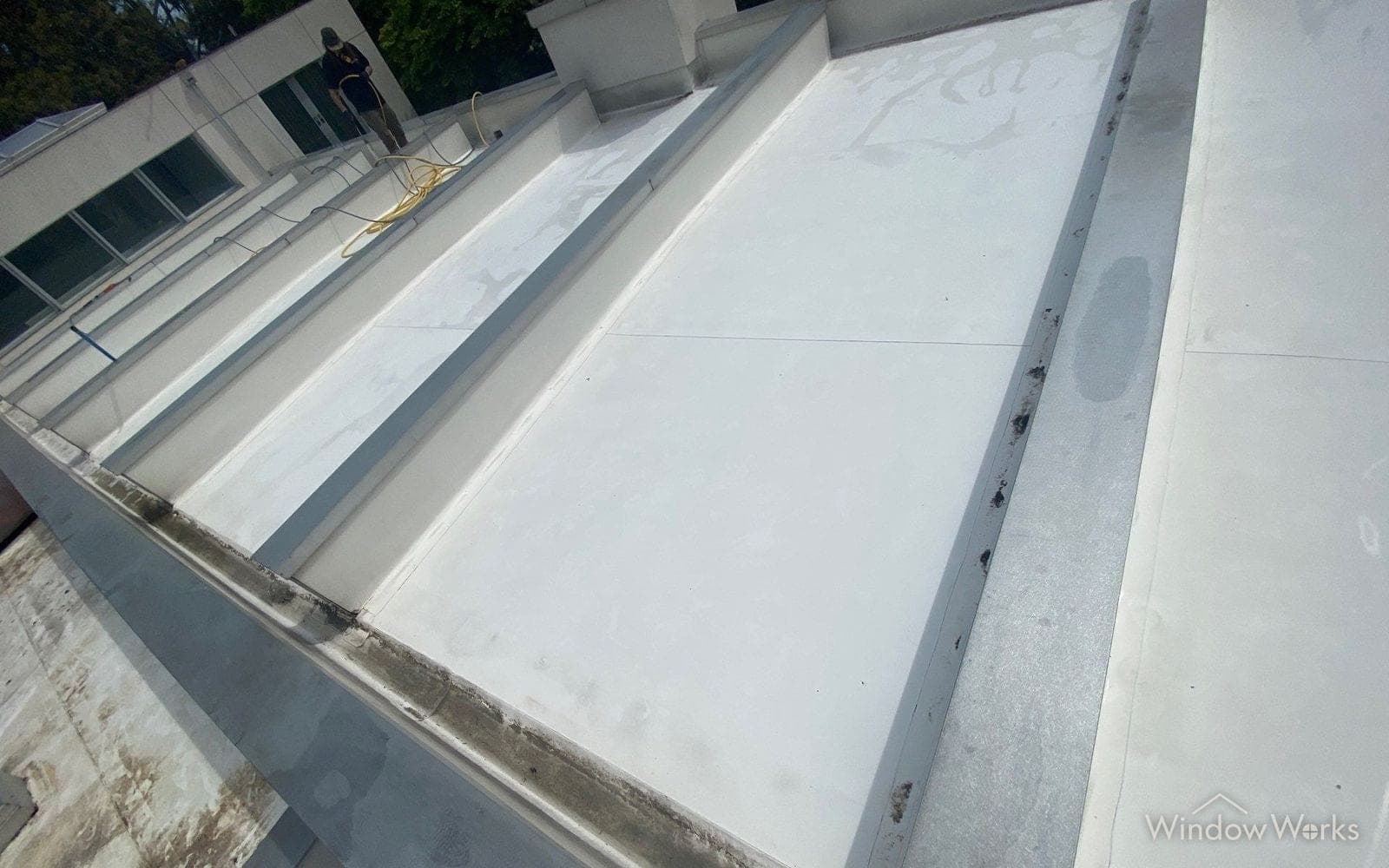 A washed white TPO membrane roof on a commercial building, the metal drainage valleys running between the panels