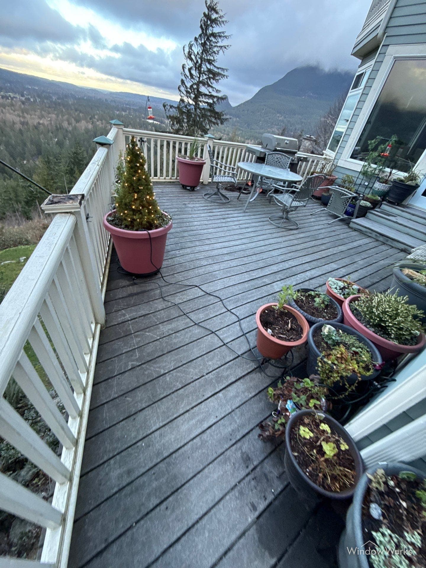 A white wood deck railing with grime-streaked pickets wrapping a weathered composite deck above a forested valley on the Eastside