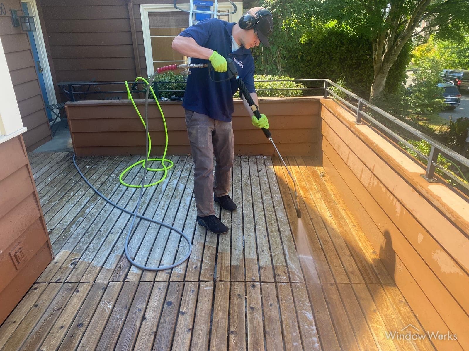 A WindowWorks technician washing a weathered wood deck, the cleaned boards showing bright against the grey ones still to do