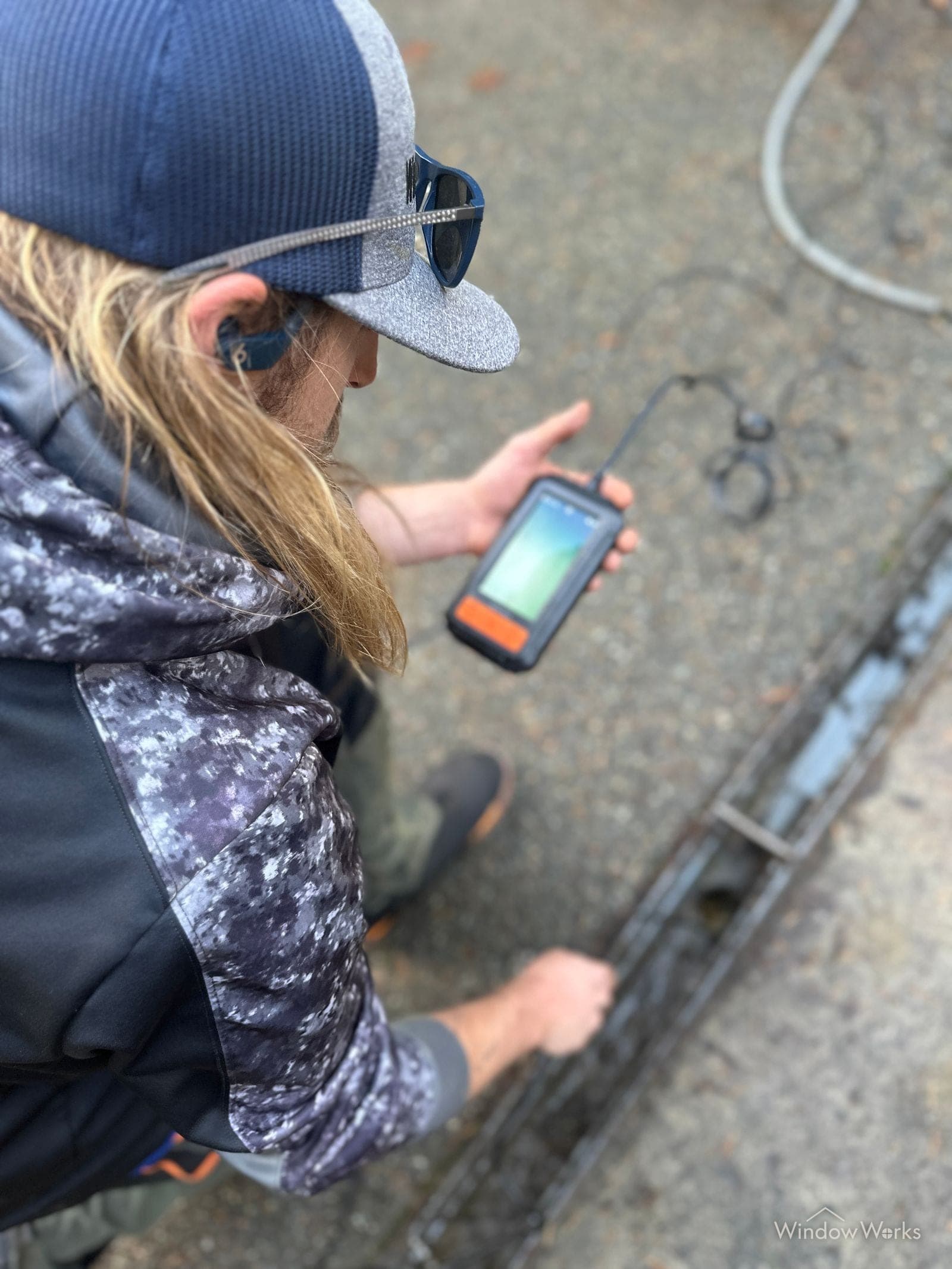 A WindowWorks technician crouched over a trench drain feeding the inspection camera line in and watching the monitor