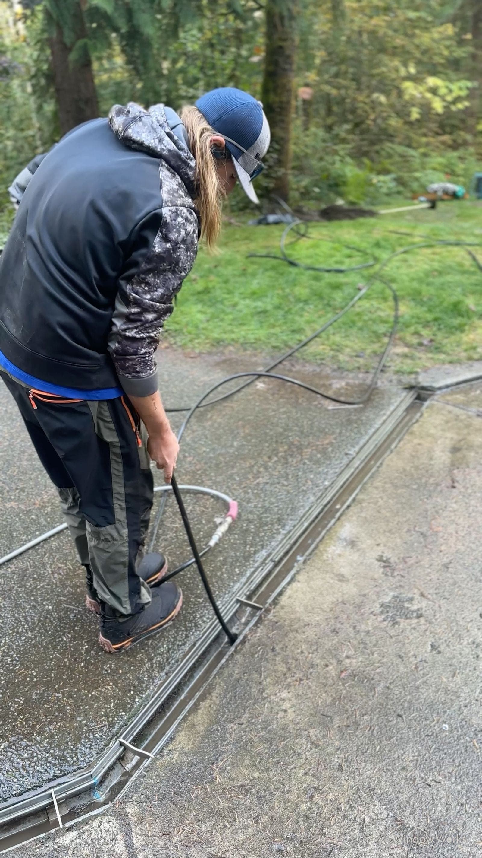 A WindowWorks technician feeding the high-pressure jetting hose into a driveway trench drain