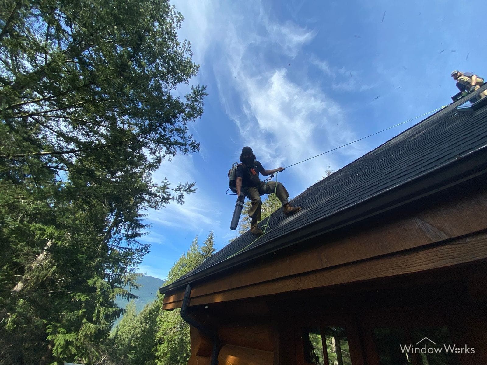 A WindowWorks technician clearing debris from a roofline gutter with a blower on the Eastside