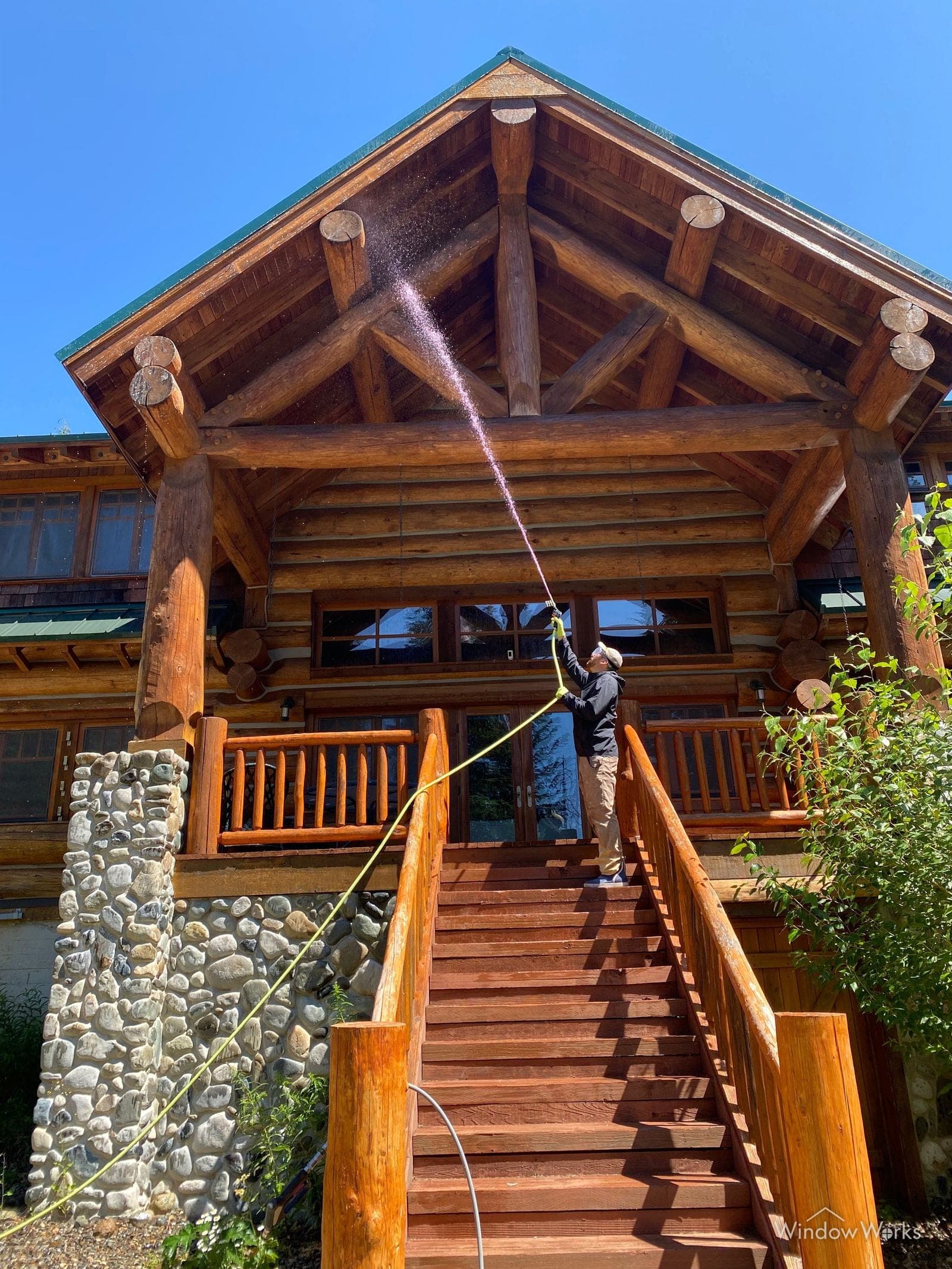 A WindowWorks technician soft washing the upper logs and gable of a log home from the entry stairs on the Eastside of Seattle