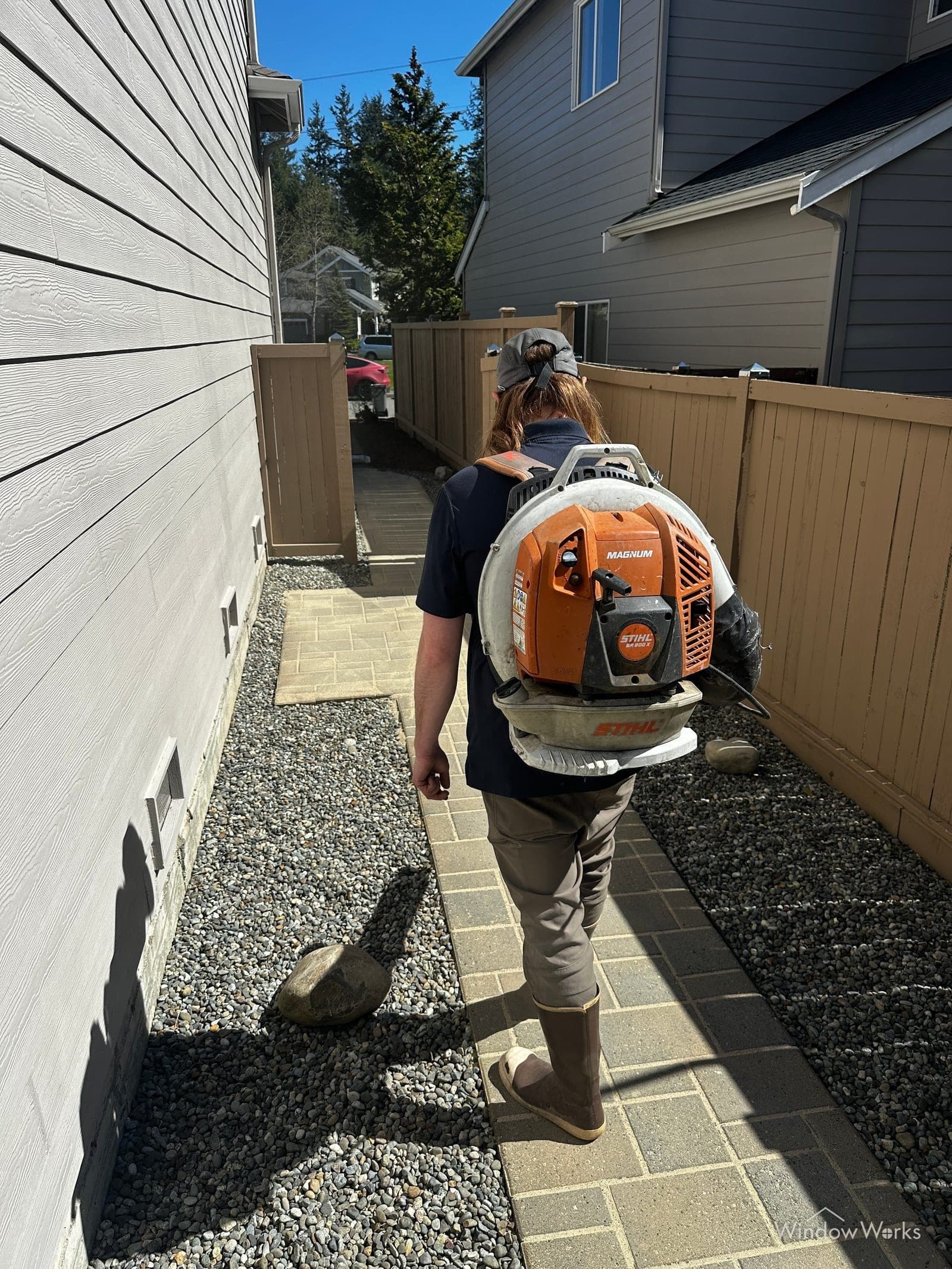 A WindowWorks technician using a backpack blower to clear and dry a freshly cleaned paver walkway at an Eastside Seattle home