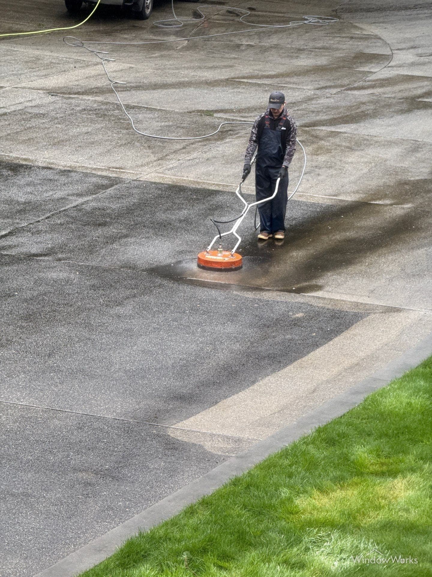 A WindowWorks technician running a surface cleaner across a concrete driveway on the Eastside of Seattle, the cleaned strip showing against the dirty concrete