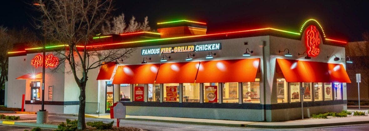 A restaurant at night with red, orange and green light bars along every roofline edge.