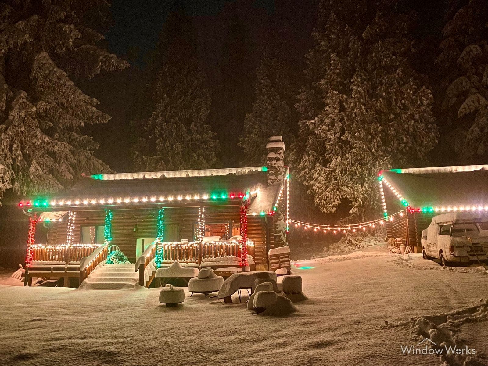 A log cabin deep in snow at night, porch and roofline run in red, green and warm white bulbs.