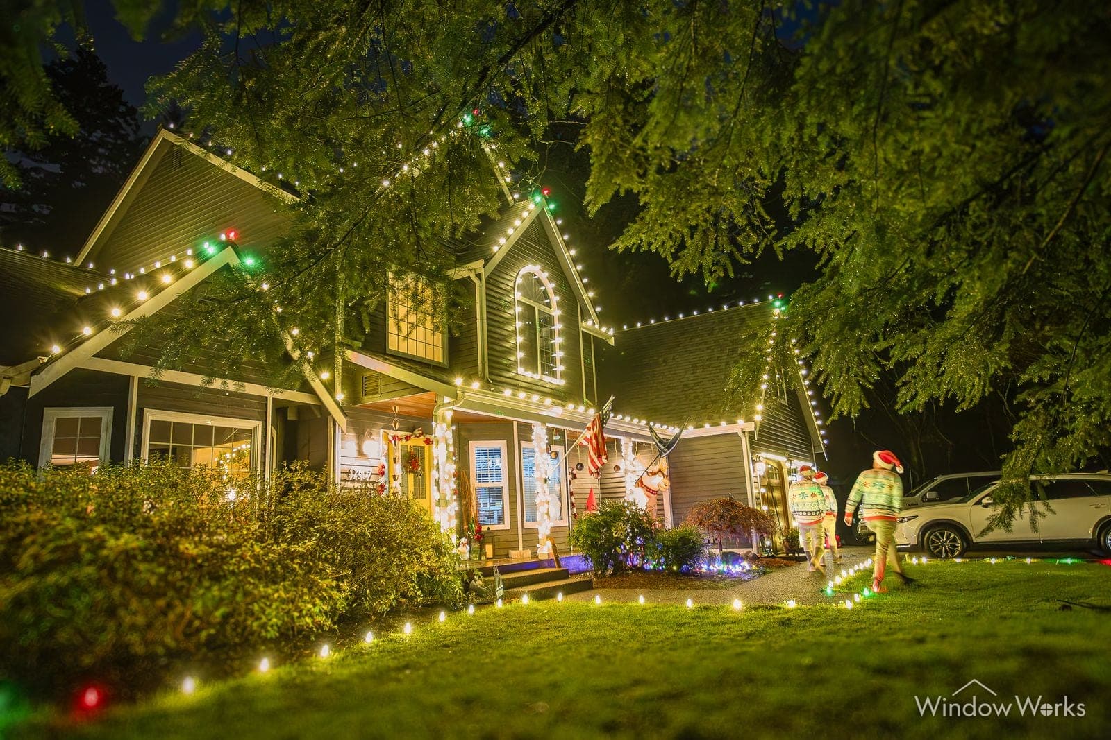 A shingled home in warm white bulbs with lit wreaths and candy canes along the walk.