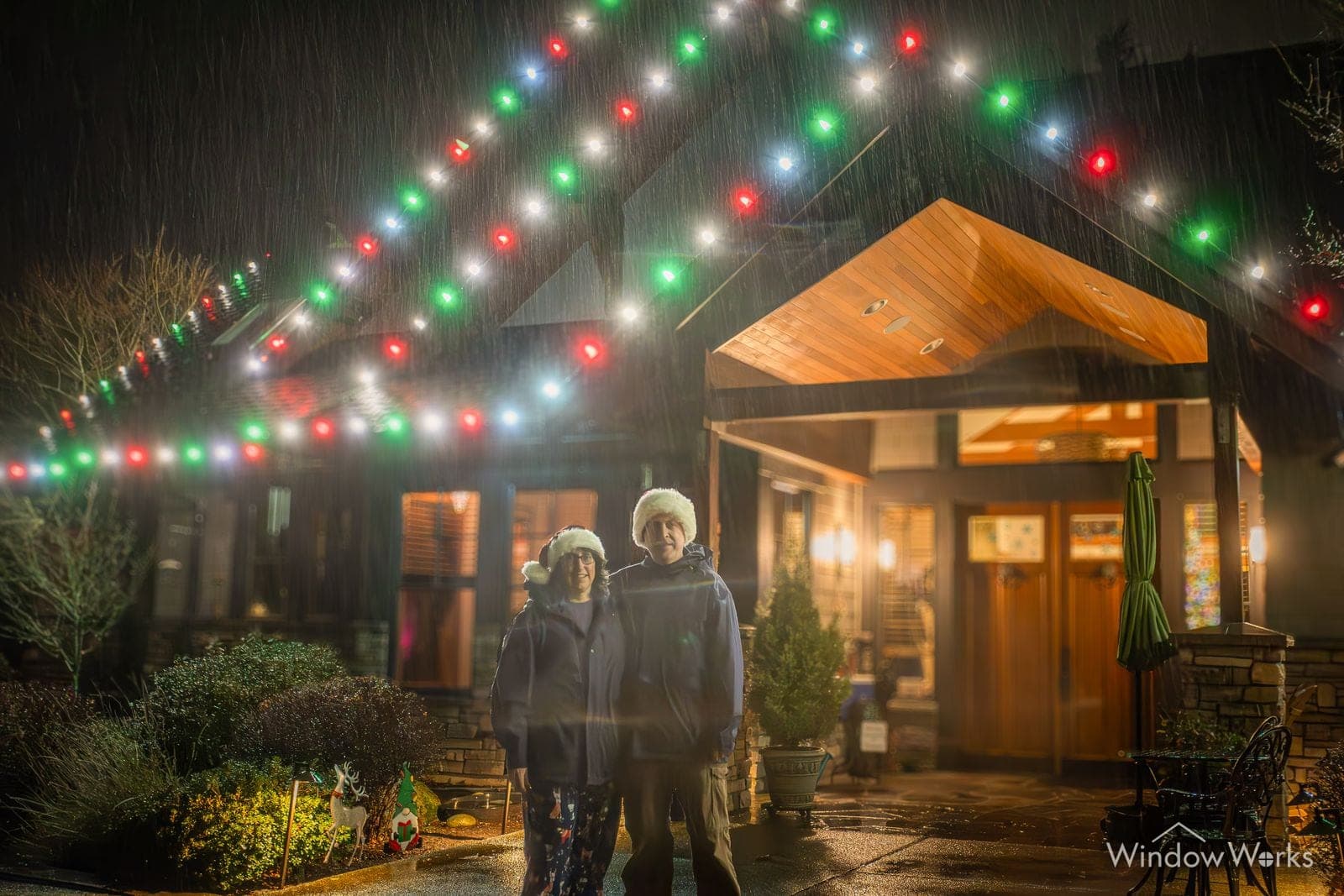 A timber entry lit in red, green and blue with two people standing under it in the rain.