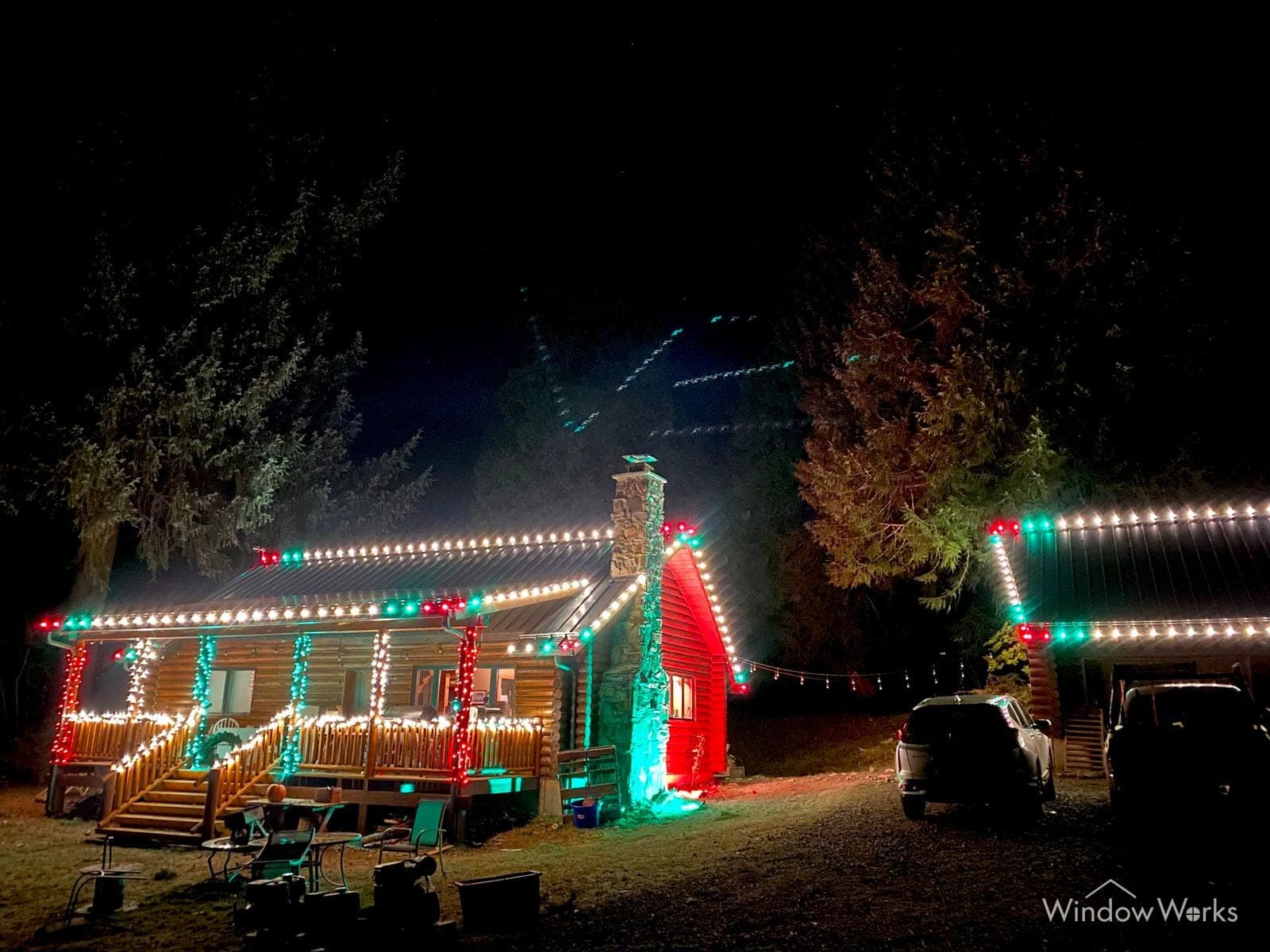 A log cabin at night in red, warm white and teal along the porch and roofline.