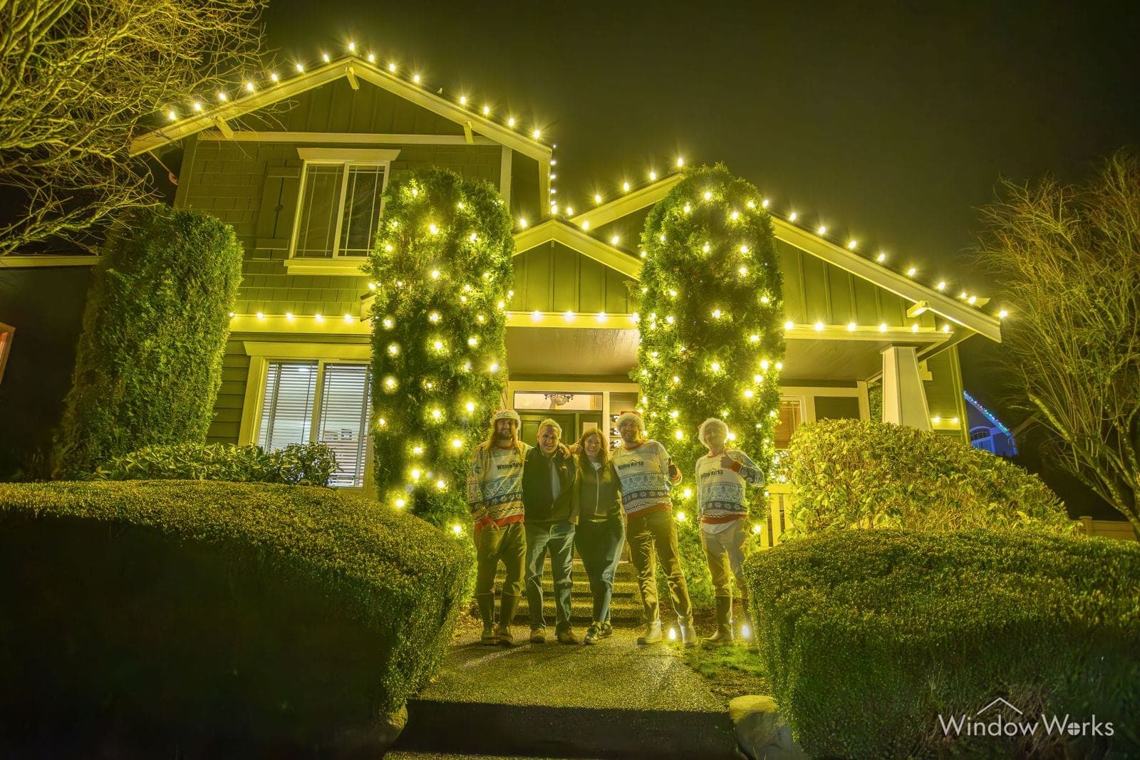 A home in warm white bulbs with lit columns either side of the door and four people standing in front.