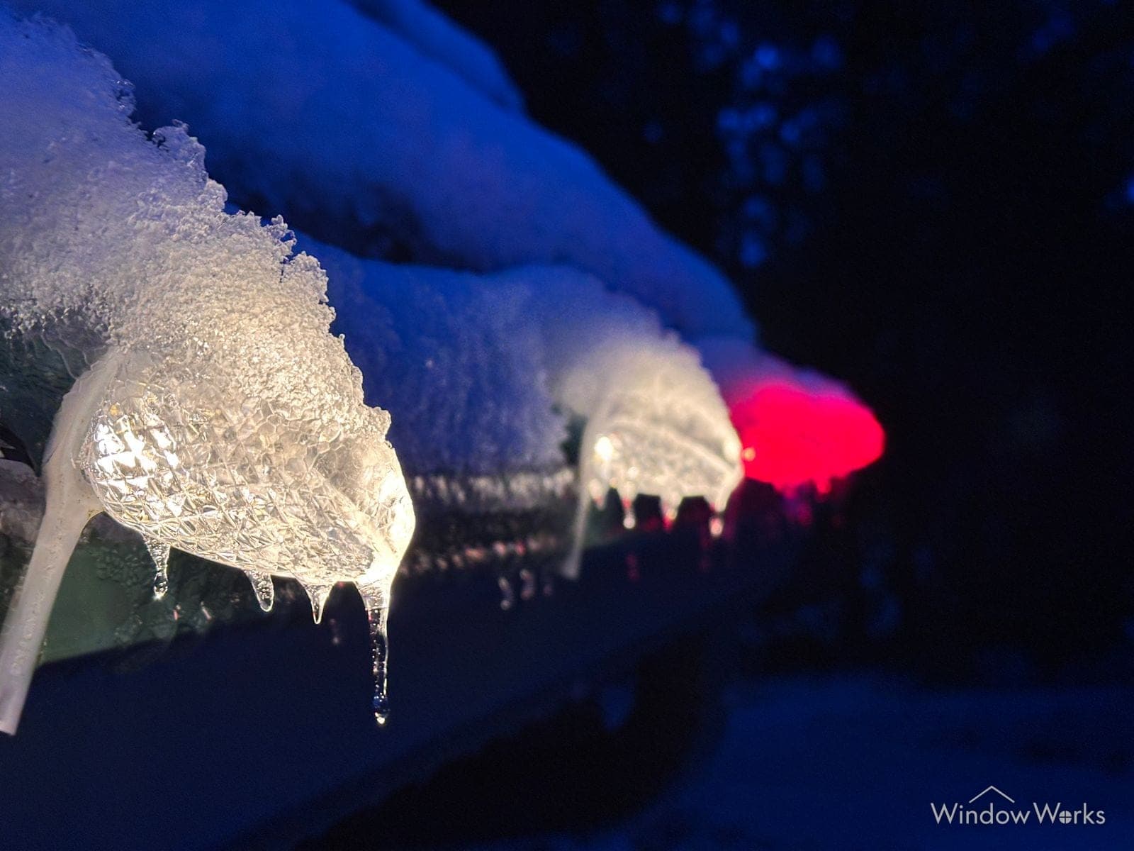 Ice formed around warm white and red bulbs on a snow-loaded eave.