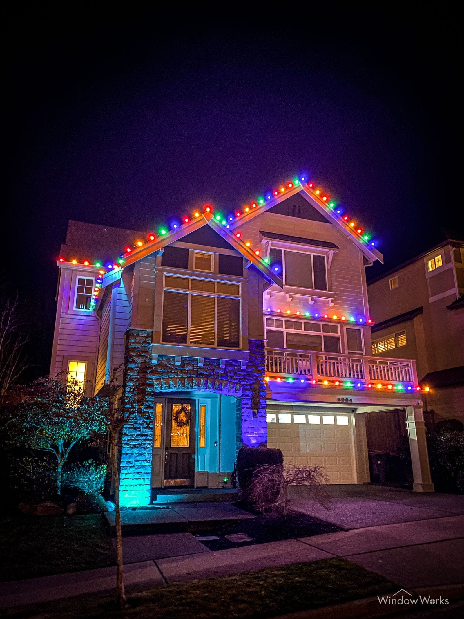 A three-story home lit magenta and teal across its balconies and entry.