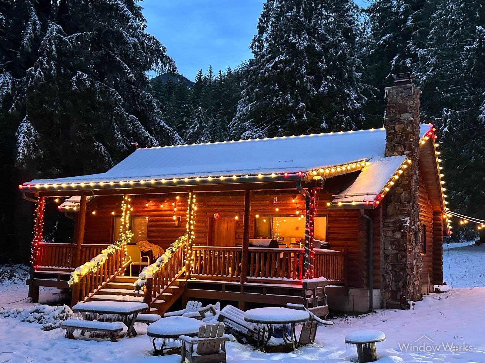 A log cabin in fresh snow, porch posts and rooflines run in multicolor bulbs.