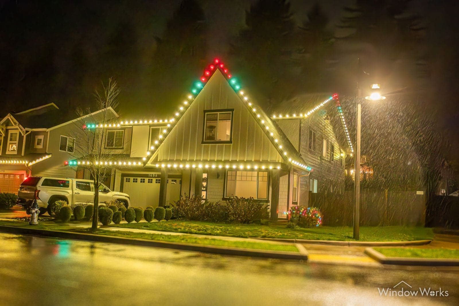 A corner home in red and green bulbs under a streetlamp on a wet night.