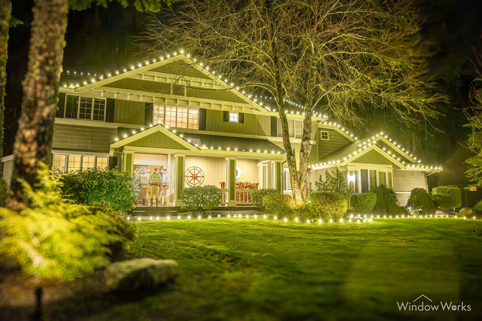A craftsman home in warm white bulbs, the lawn washed green from the bed lighting.