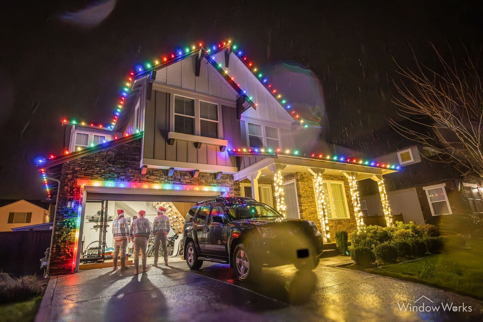 A group on the drive beside a truck, the home behind them run in multicolor bulbs.