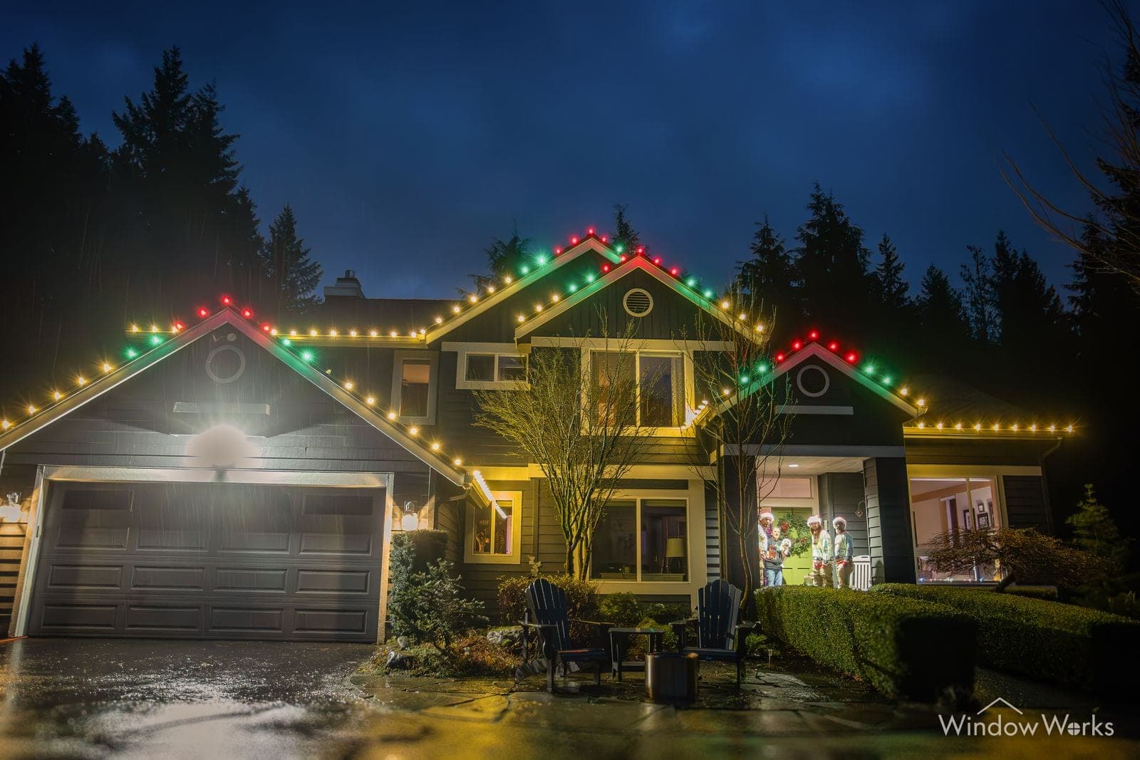 A dark-sided craftsman in red, green and warm white bulbs above a lit garage.