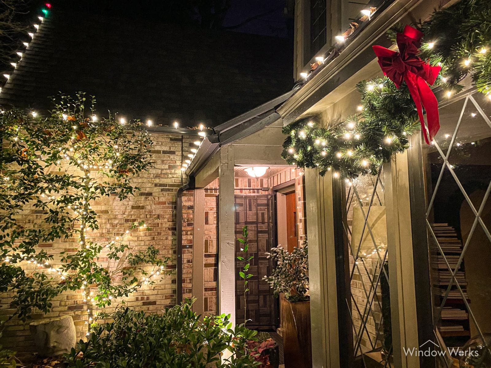 A stone entry with lit garland up the stair rail, a wreath and an oversized red bow overhead.