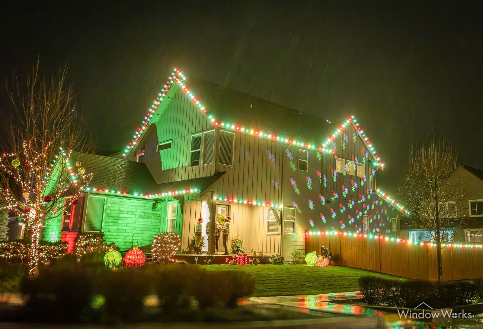 A green home in red and white bulbs with lit shrubs and a wrapped tree at the corner.