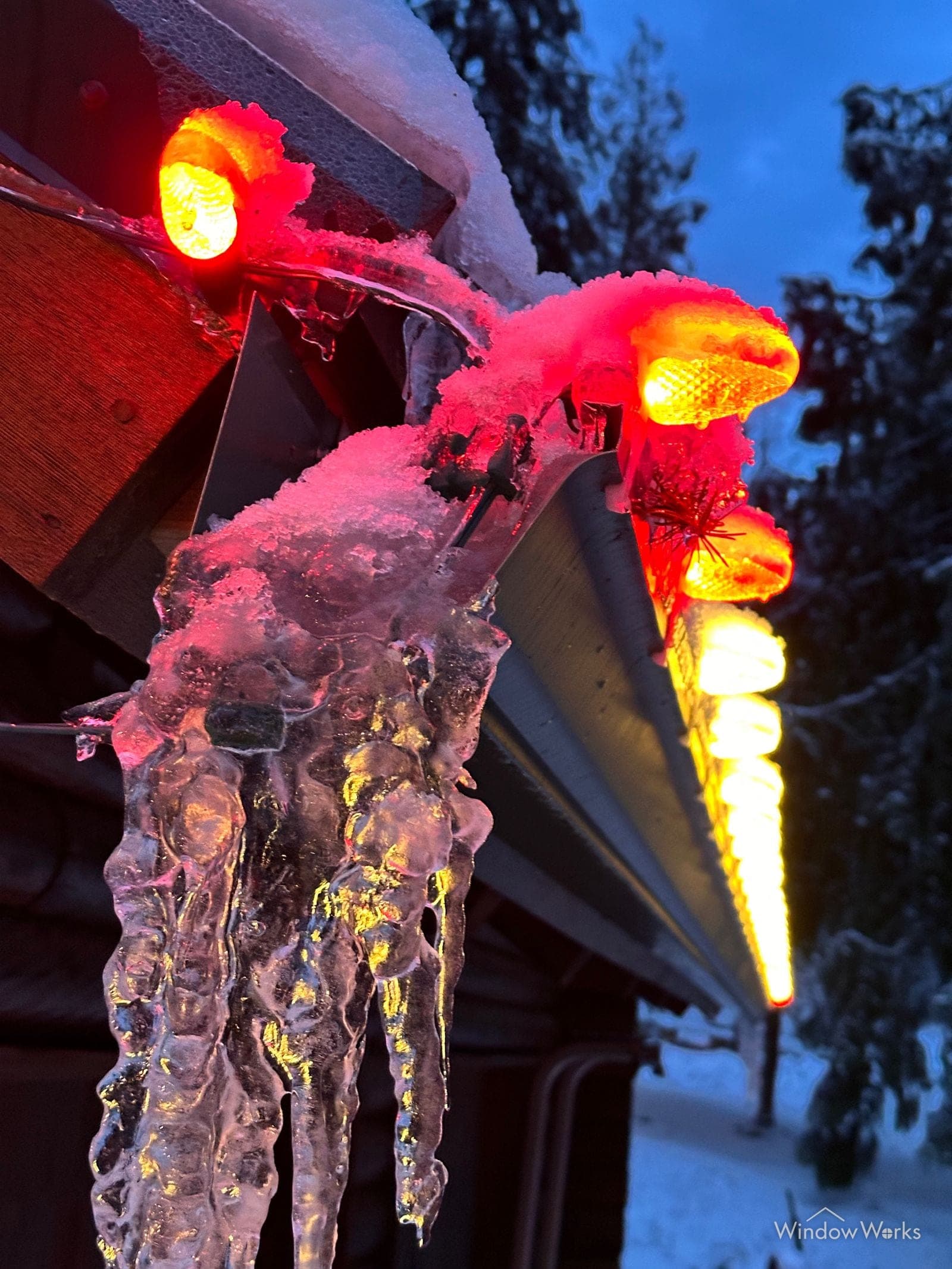 Icicles hanging from a lit eave, glowing red around a warm bulb line.