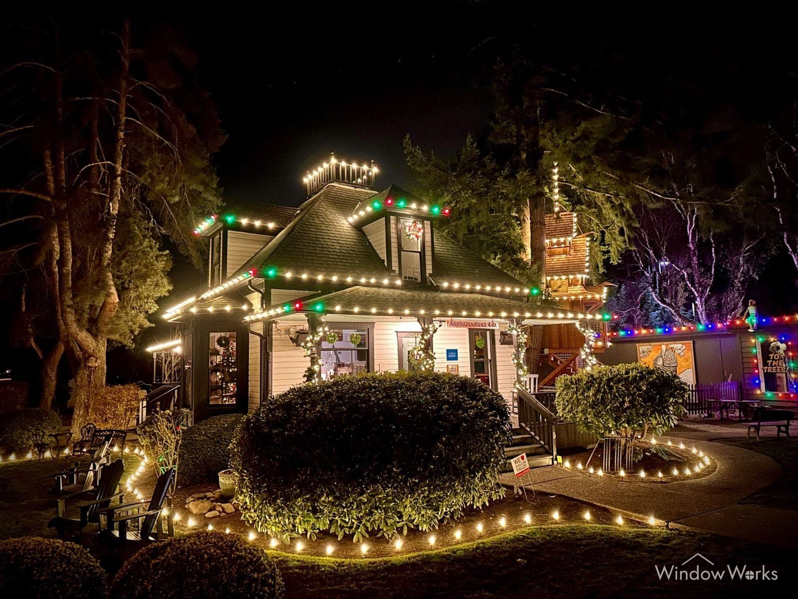 A home at night in multicolor bulbs with the clipped hedges and the walk below lit warm white.
