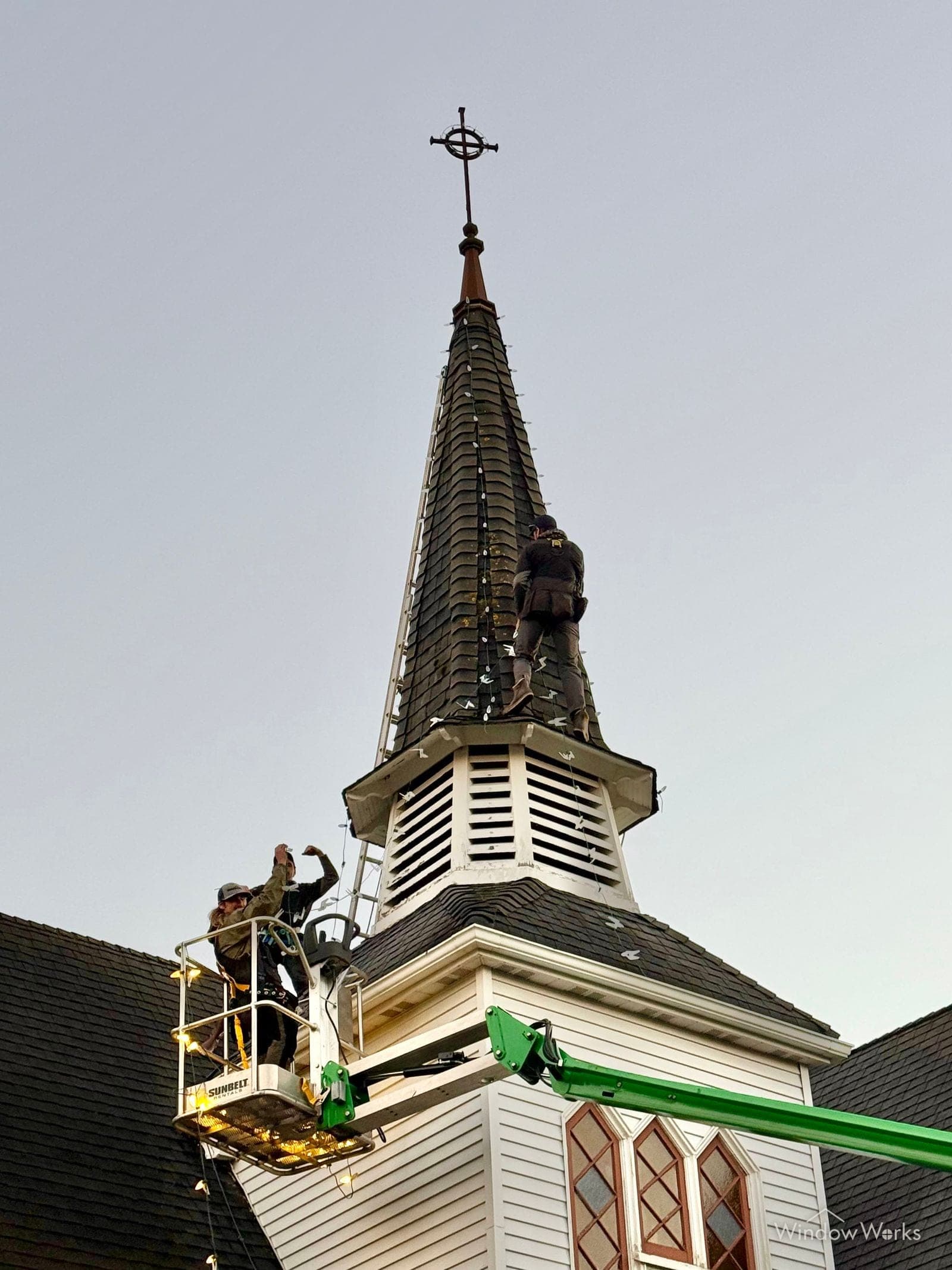A technician in a boom lift working at the top of a church steeple.