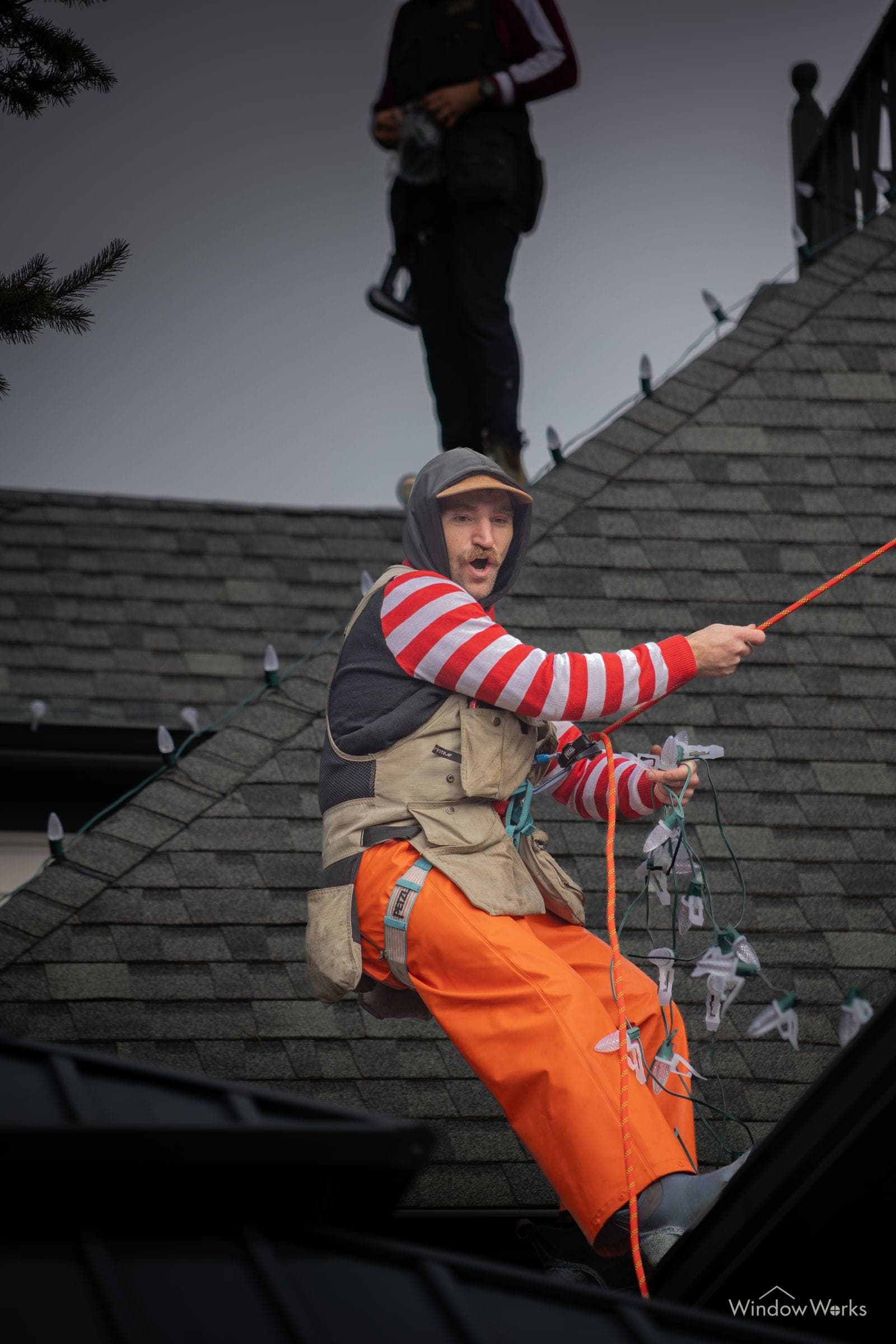 Two technicians working a steep roof together, one feeding the light line up to the other.