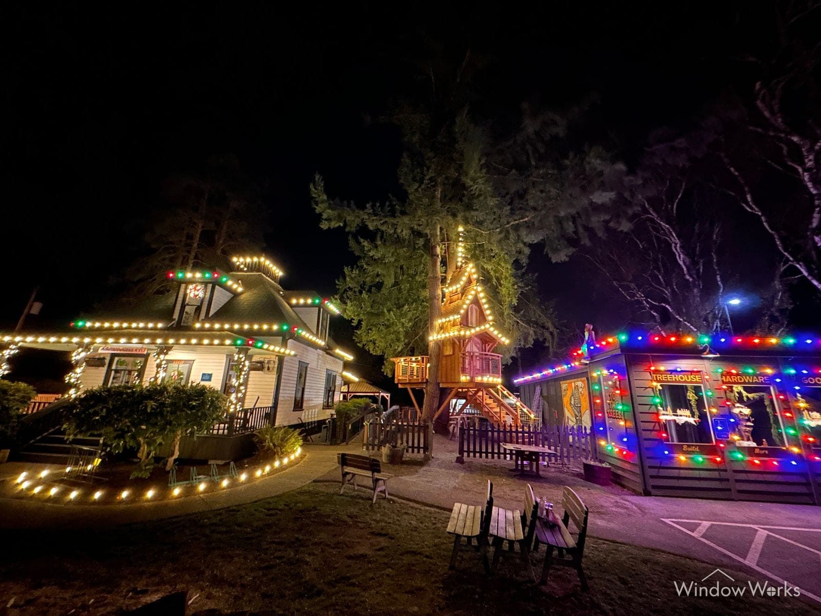 A back garden at night with the house, a two-story playhouse and a garden bar all outlined in multicolor C9 bulbs, warm bulbs edging the lawn past the picnic table and chairs.
