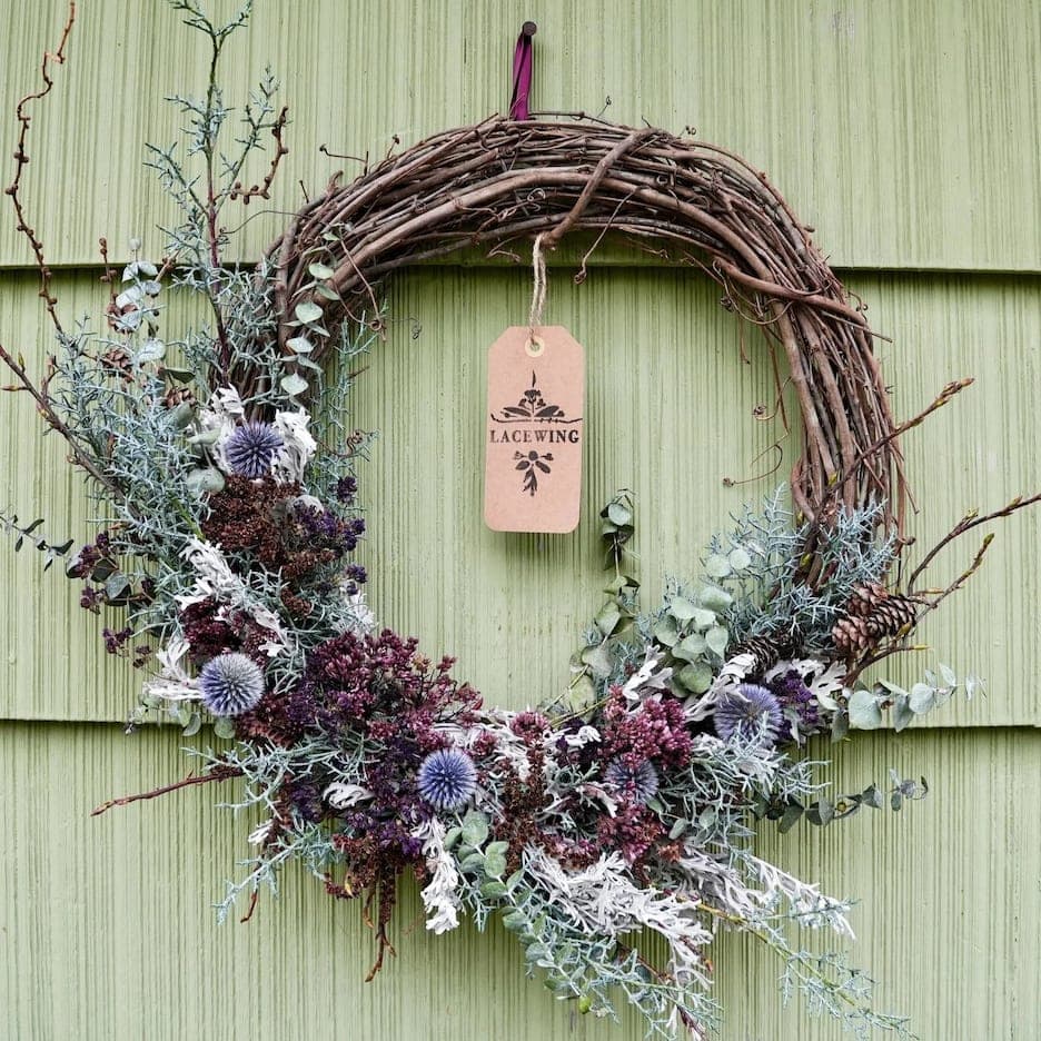 A modern wreath on a grapevine base, dried seed heads, thistle and pale blooms worked through fresh evergreen.