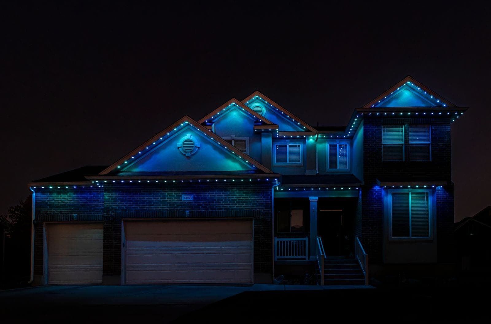 The same home running blue and teal, the gables lit cool and the garage bays washed pale blue.