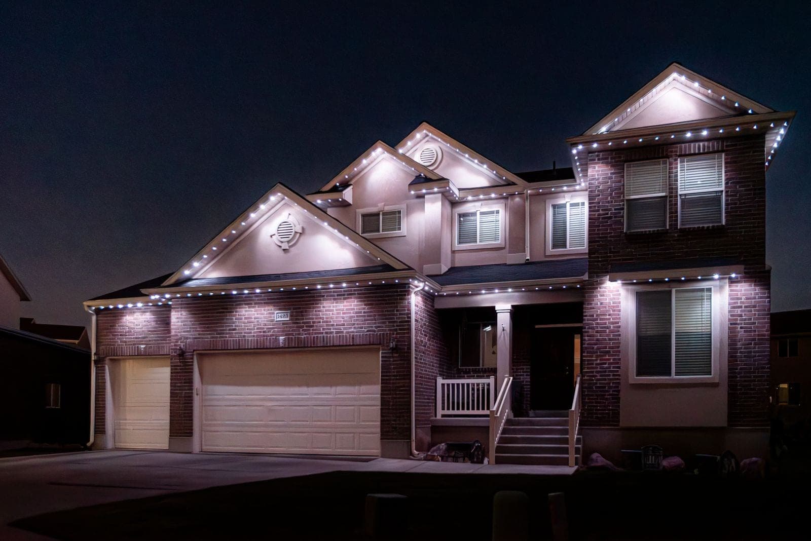 The same home running warm white along every roofline, the everyday setting seen wide.