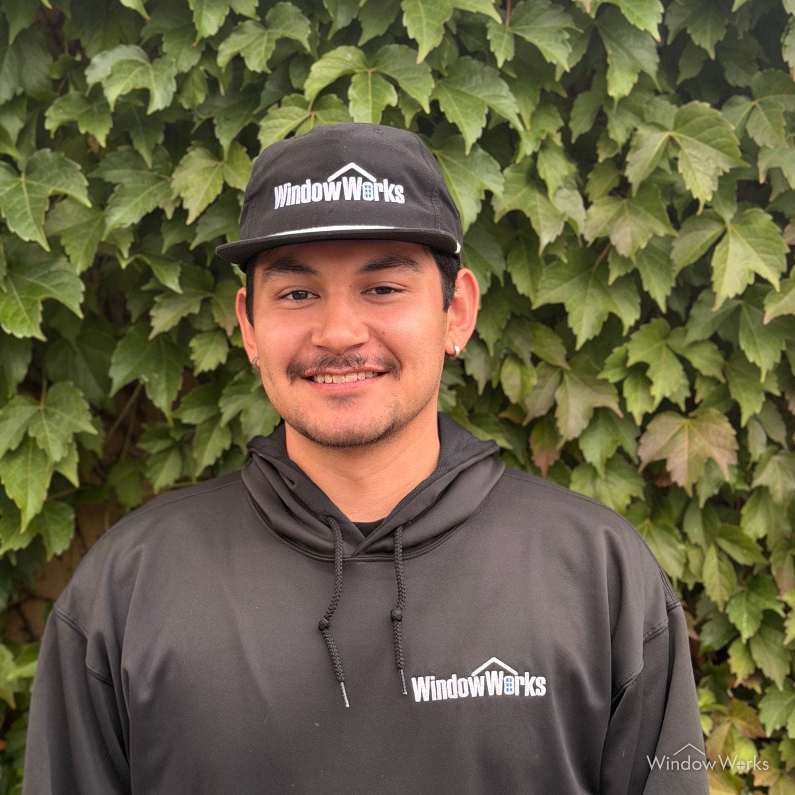Noa H., Field Technician at WindowWorks, in uniform in front of an ivy wall