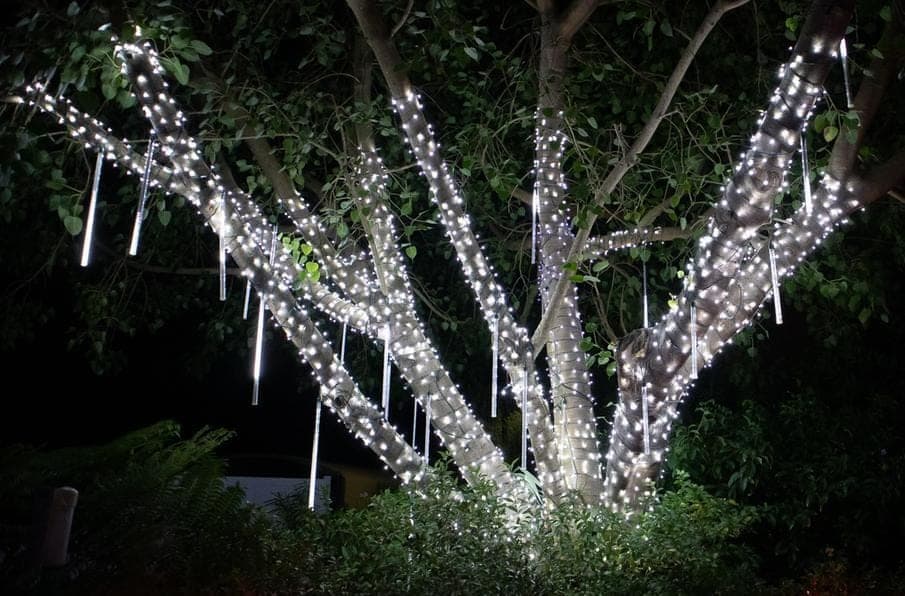 Snowfall tubes dripping white light through a tree wrapped in pure white minis at night.