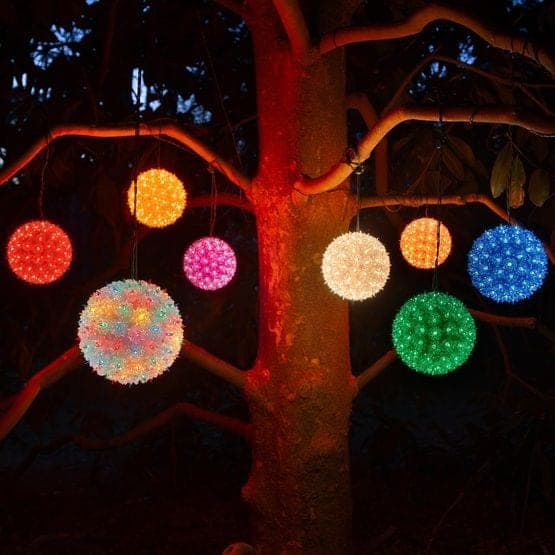 Lit spheres in red, green, blue and multicolor hanging through the bare branches of a tree at night.