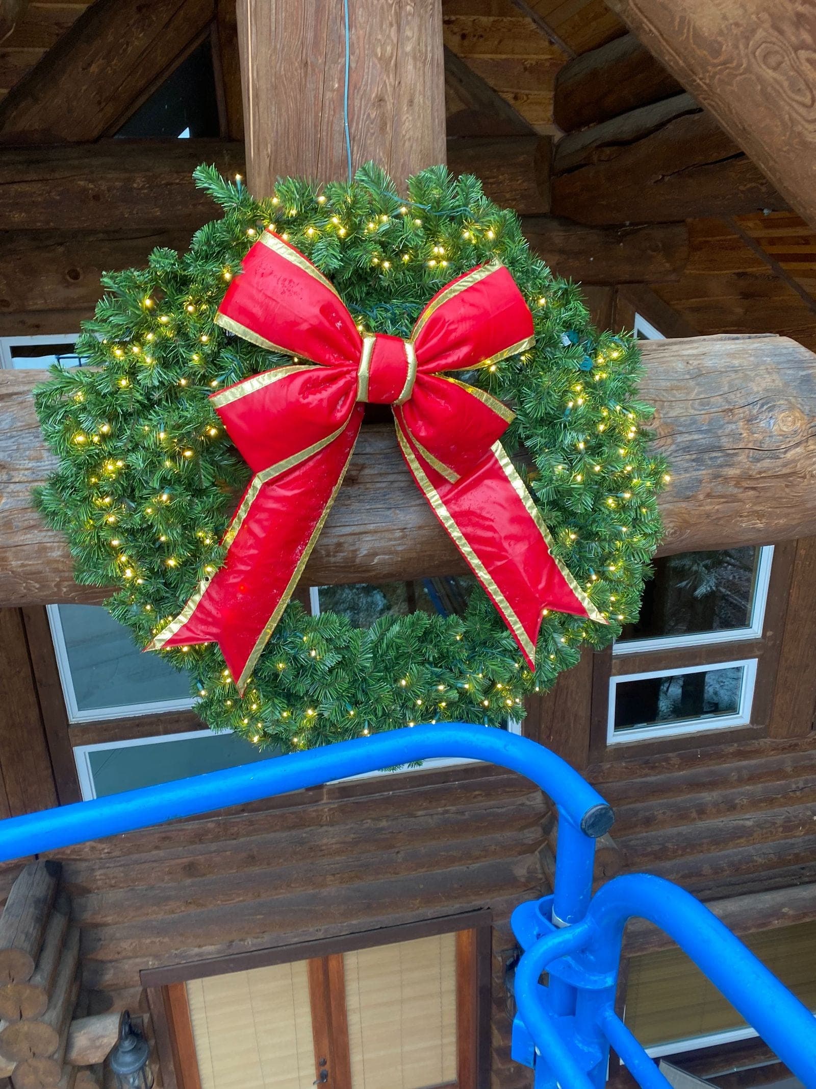 A lit evergreen wreath with a red bow hung on a timber gable, photographed from the lift during install.