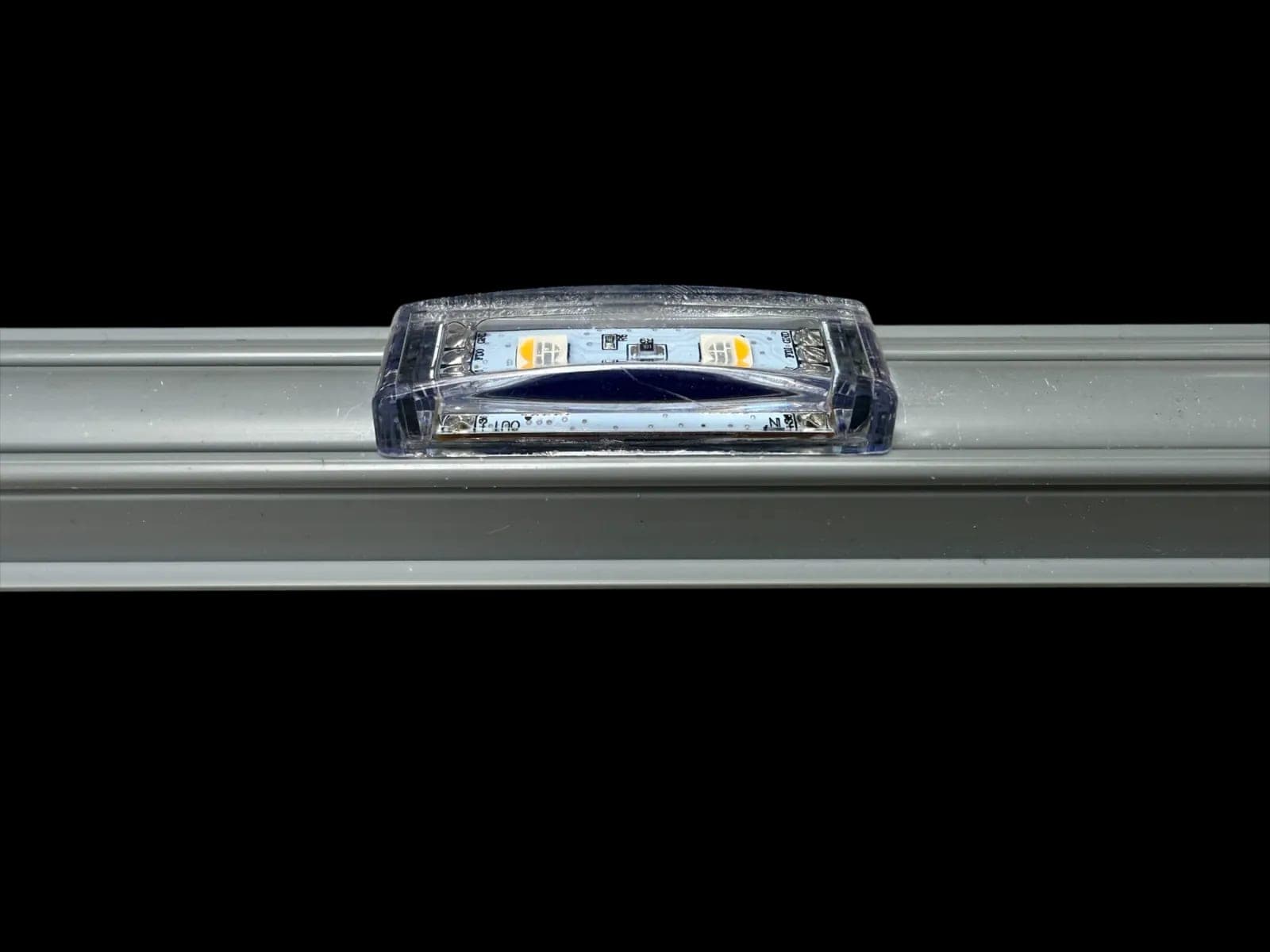 A single LED module seated in an aluminum mounting channel, lit warm white.