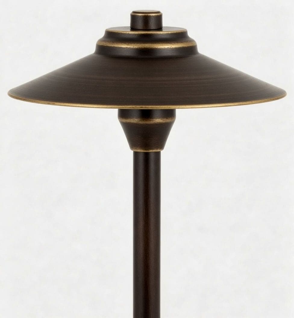 A bronze path light with a wide hat shade on a slim stem, shown against a plain pale background.