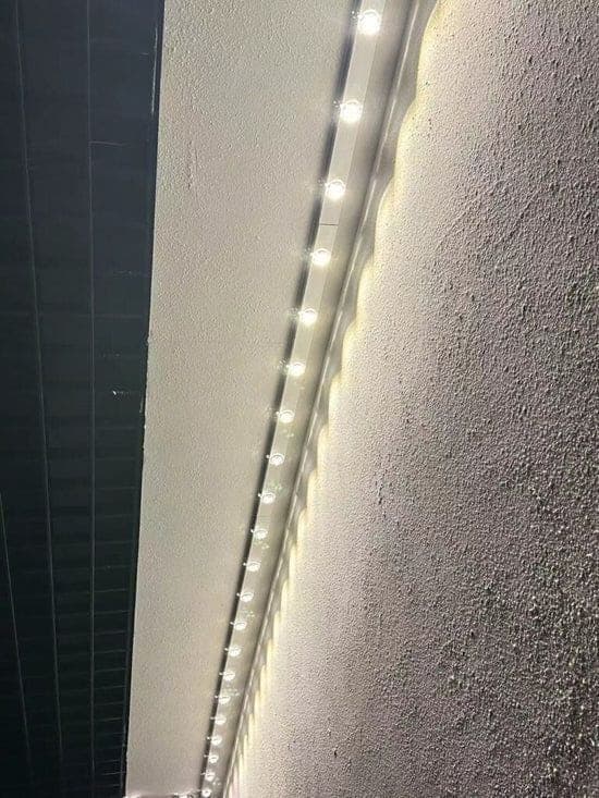 A run of puck lights down an exterior corner washing a textured wall in warm white.
