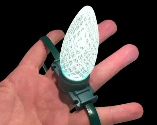 A faceted RGB C9 bulb clipped to a green wire, held in a hand and lit pale green.