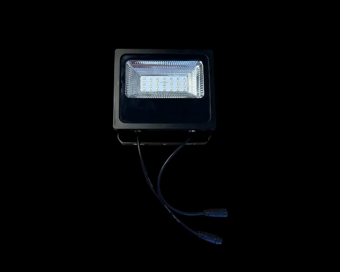 A compact RGB flood light fixture with its lens and lead wire against black.