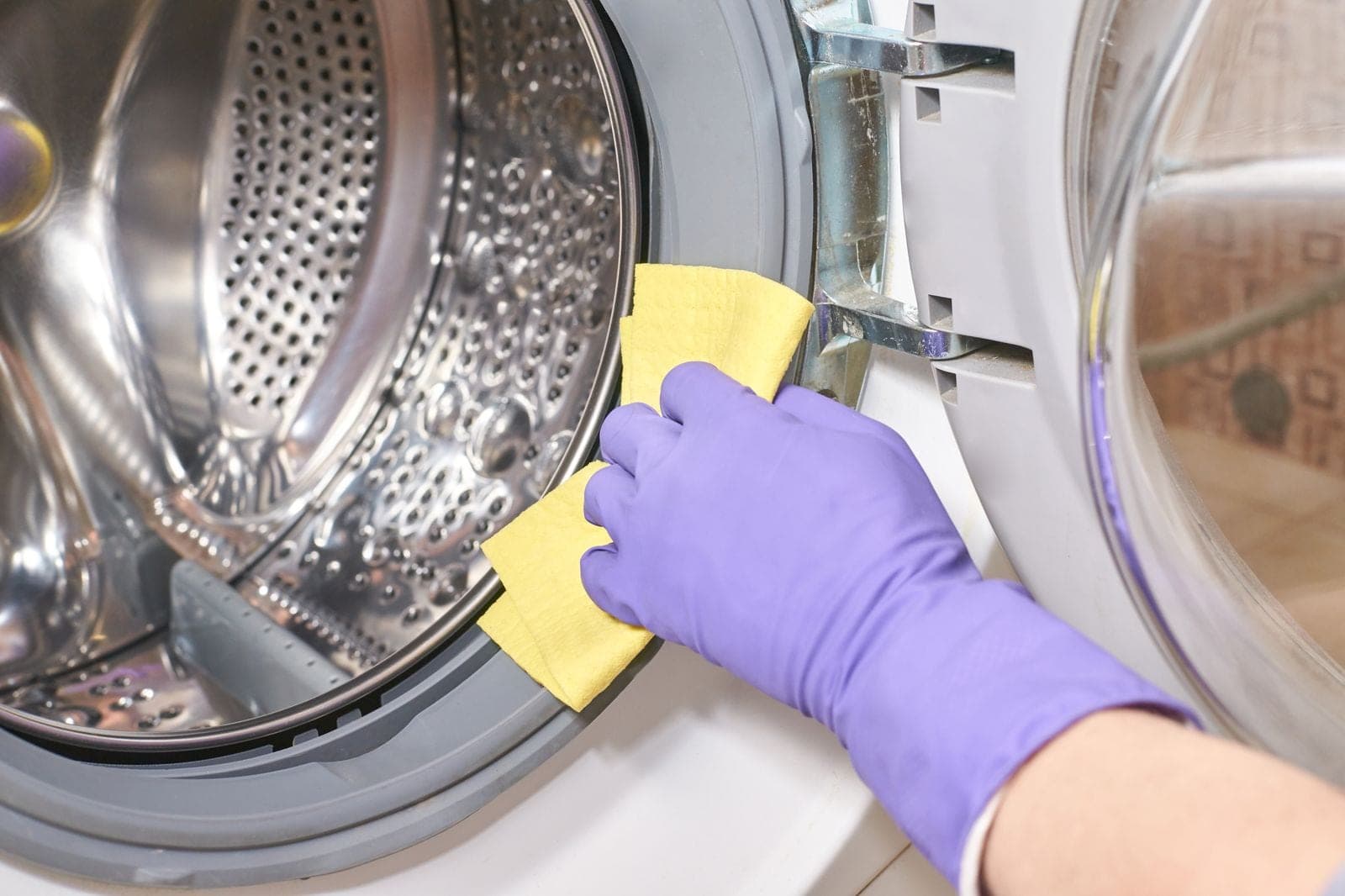 A gloved hand wiping the rubber door seal of a front-loading washing machine with a cloth