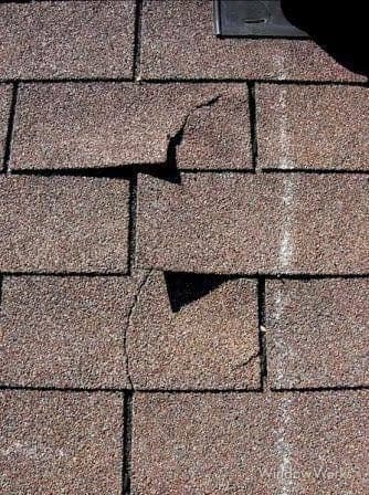 A cracked and split asphalt shingle with a gap exposing the layer beneath.